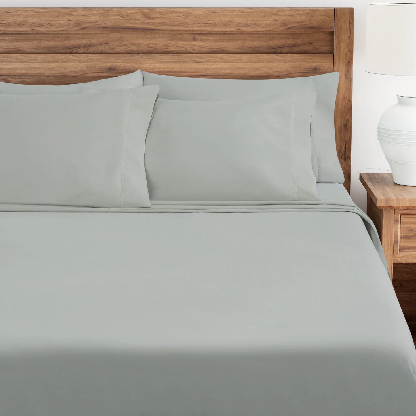 Oystershell bed sheets and pillows on a wooden bed with a white nightstand.