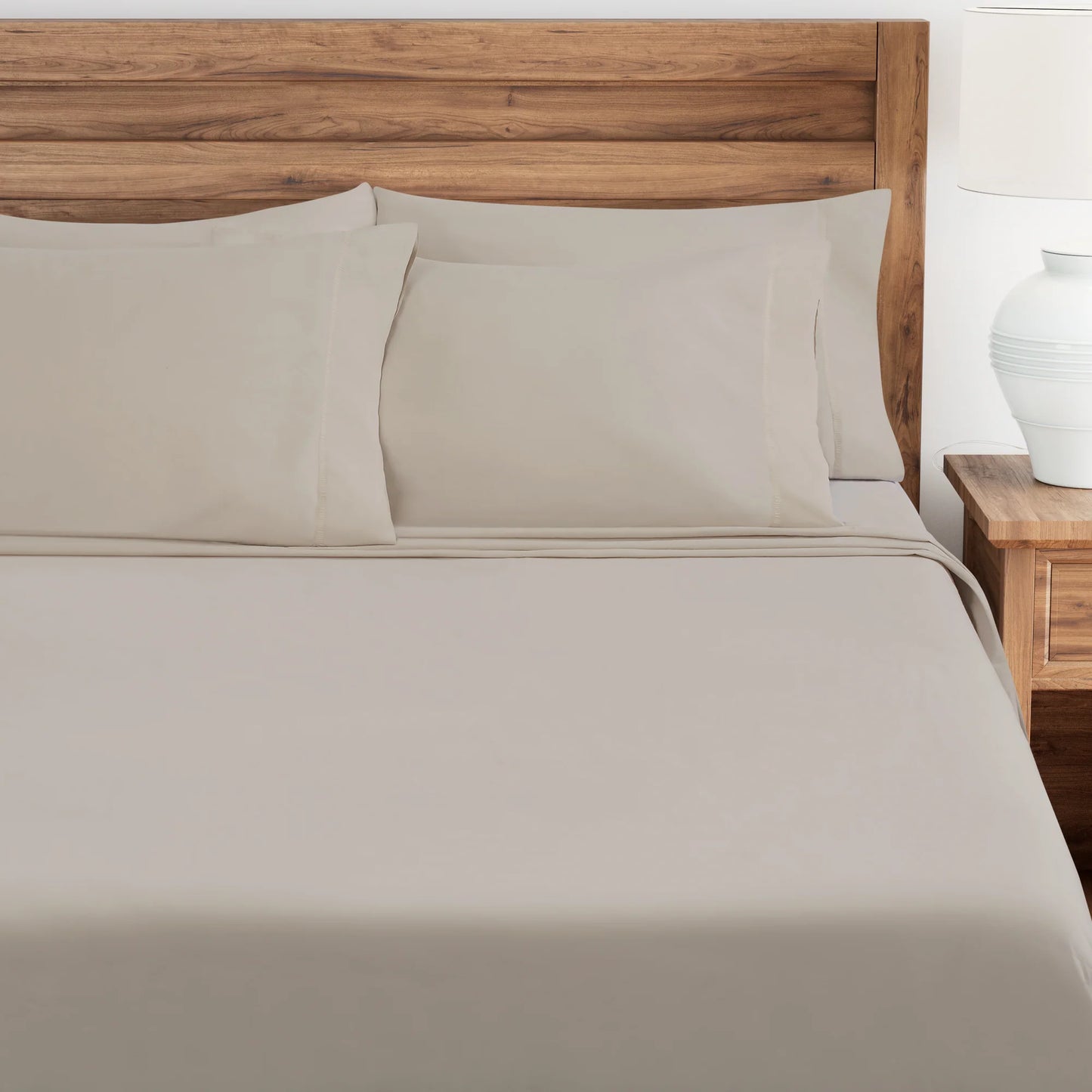 Punice Stone bed sheets and pillows on a wooden bed with a nightstand in the background.