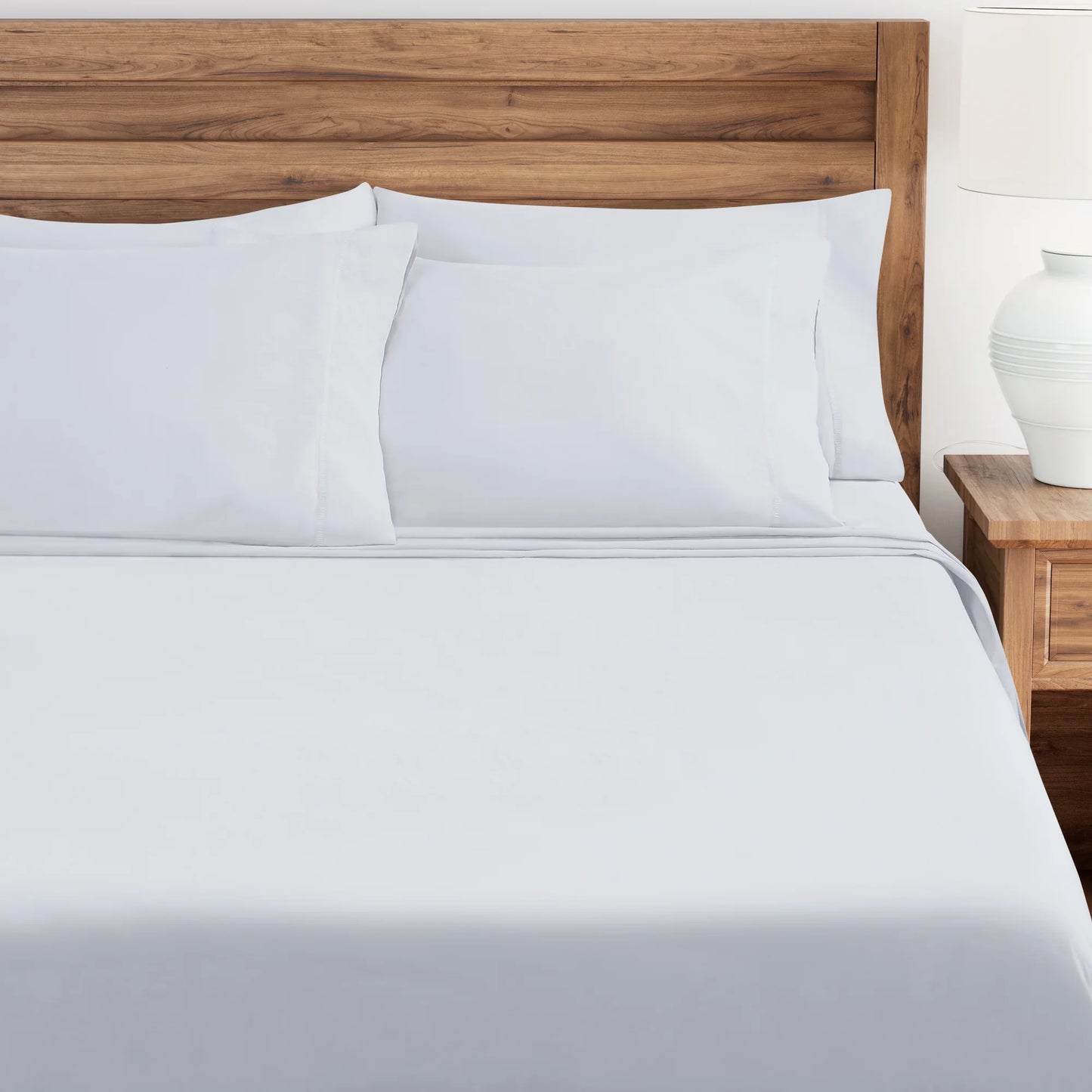 White bedding set on a bed with a wooden headboard and nightstand.